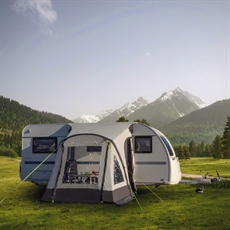 Fortelt med gjennomsiktige vinduer og grønne barduner, festet til campingvogn i fjellandskap.